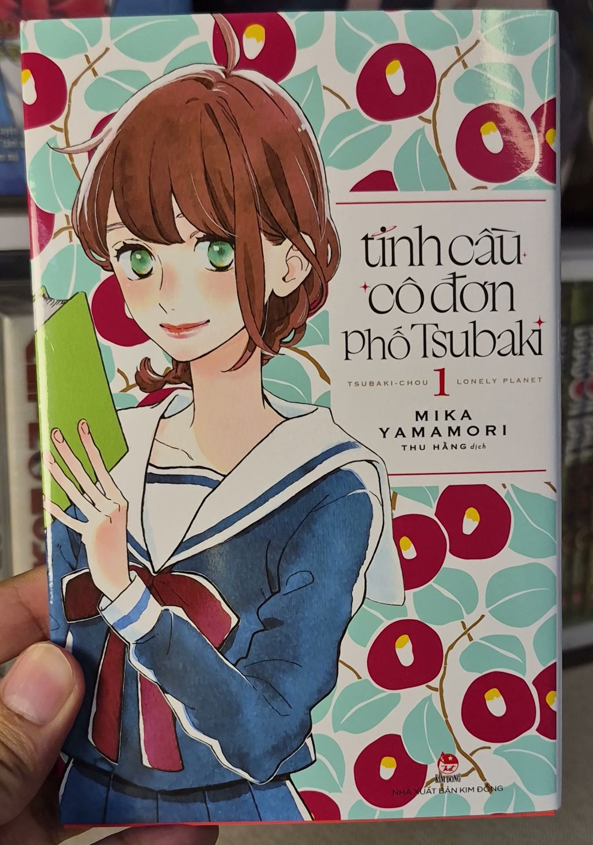 Bìa Tinh cầu cô đơn phố Tsubaki manga tập 1 với Fumi mặc đồng phục thủy thủ trước nền hoa trà đỏ